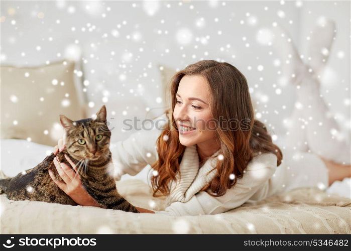 pets, comfort, christmas, winter and people concept - happy young woman with cat lying in bed at home over snow. happy young woman with cat lying in bed at home