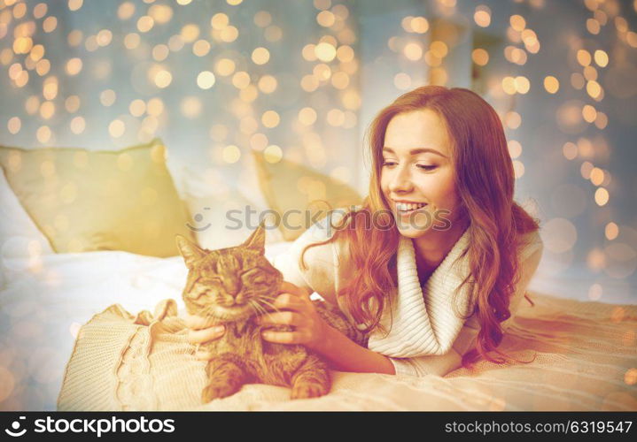 pets, comfort, christmas, winter and people concept - happy young woman with cat lying in bed at home. happy young woman with cat lying in bed at home