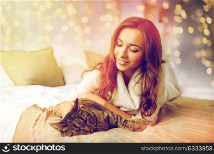pets, comfort, christmas, winter and people concept - happy young woman with cat lying in bed at home. happy young woman with cat lying in bed at home