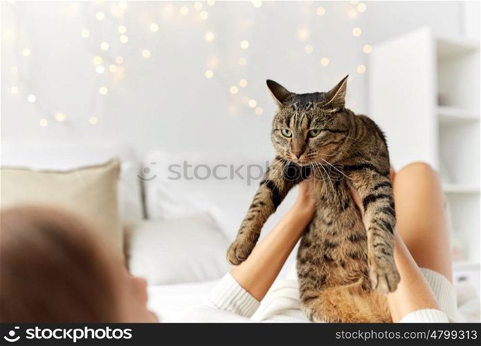 pets, comfort, christmas, winter and people concept - young woman with cat lying in bed at home