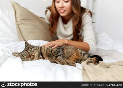 pets, comfort, rest and people concept - happy young woman with cat lying in bed at home