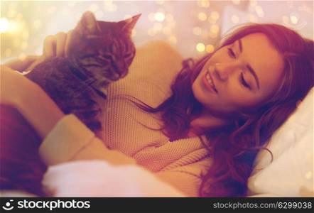 pets, comfort, rest and people concept - happy young woman with cat lying in bed at home at night. happy young woman with cat lying in bed at home