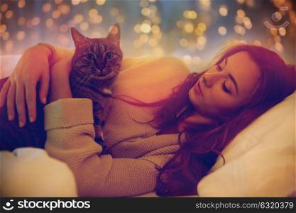 pets, comfort, rest and people concept - happy young woman with cat lying in bed at home at night. happy young woman with cat lying in bed at home