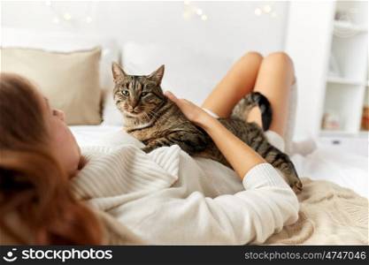 pets, comfort, rest and people concept - young woman with cat lying in bed at home