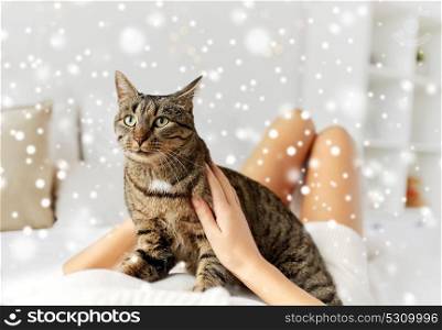 pets, comfort, winter and people concept - young woman with cat lying in bed at home over snow. young woman with cat lying in bed at home