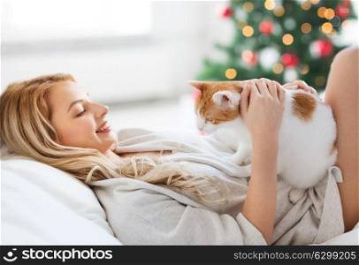pets, holidays and people concept - happy young woman with cat in bed at home over christmas tree background. happy young woman with cat in bed at christmas