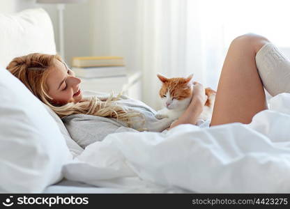 pets, morning, comfort, rest and people concept - happy young woman with cat in bed at home