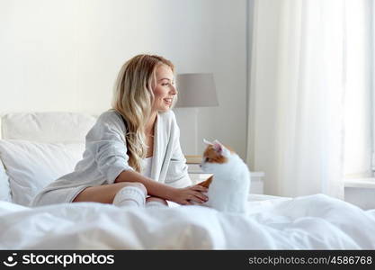 pets, morning, comfort, rest and people concept - happy young woman with cat in bed at home