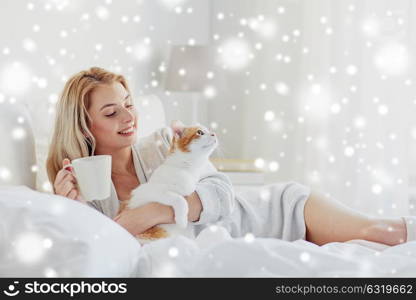 pets, morning, comfort, rest and people concept - happy young woman with coffee cup and cat in bed at home over snow. happy woman with coffee and cat in bed at home