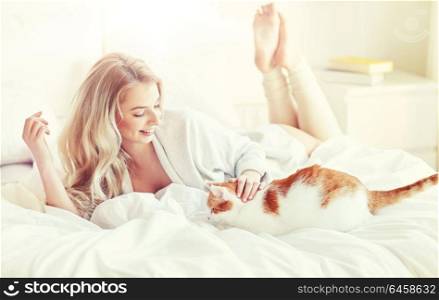 pets, morning, comfort, rest and people concept - happy young woman with cat in bed at home. happy young woman with cat in bed at home