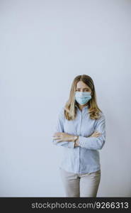 Petty young business woman with protective face mask stands by the wall in the office