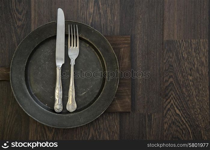 Pewter plate and vintage cutlery on rustic wooden background