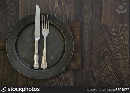 Pewter plate and vintage cutlery on rustic wooden background