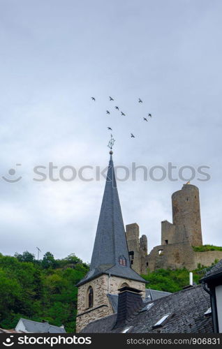 Pfarrkirche church and Lowenburg castle with flying birds in the background at the picturesque village of Monreal in the Eifel region, Germany