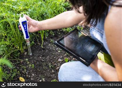PH meter tester in soil. Measure soil with digital device and tablet. Woman farmer in a garden. Concept for new technology in the agriculture.