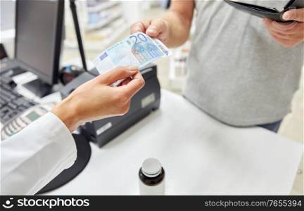 pharmaceutics, healthcare and people concept - close up of customer buying medicine and paying money to pharmacist at pharmacy. pharmacist taking money from customer at pharmacy
