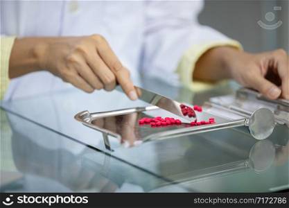Pharmacist counting medicine in stainless steel containers on the table close up to sport focus