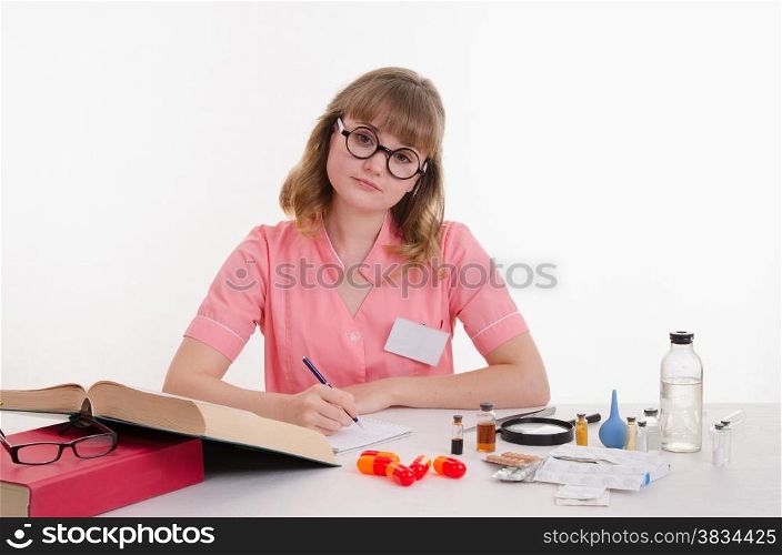 Pharmacist sitting at the table reading a thick handbook of medicines