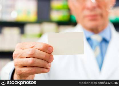 Pharmacist with business card in pharmacy; focus on card