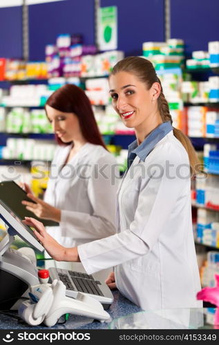 Pharmacist with female assistant in pharmacy standing at the cashpoint