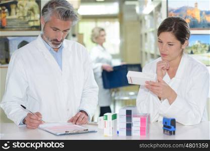 pharmacists standing at counter and showing medicine box in pharmacy