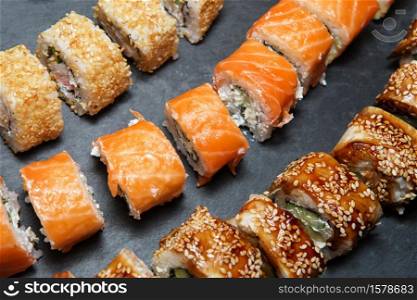 Philadelphia Roll, California Roll, Eel Avocado Roll on black slate tray background. Delicious rolls and sushi with eel, salmon, shrimp, cucumber and philadelphia. Various delicious Types of Sushi Rolls. Top view, flat lay