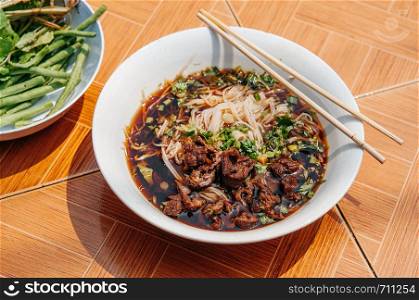 Pho Laos black herbal soup beef noodle, Luang Prabang local street food with side vegetables bowl.