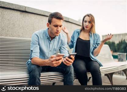 Phone addict man with two gadgets ignoring his woman. Social addicted people, problems in relationships