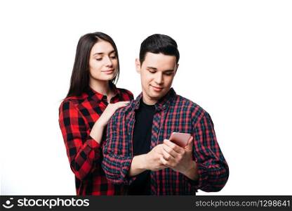 Phone addicted couple, white background. Woman hugs man that looking on smartphone screen
