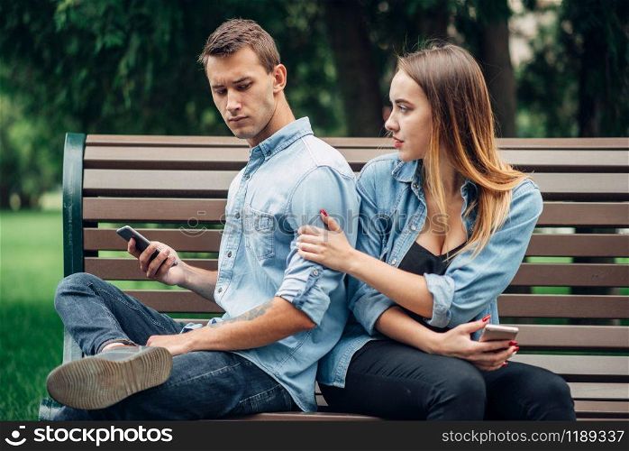 Phone addicted people, man using smartphone and ignoring his woman, couple in summer park, social addict. Phone addicted people, man ignoring his woman
