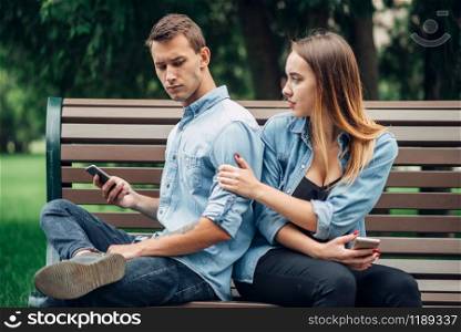 Phone addicted people, man using smartphone and ignoring his woman, couple in summer park, social addict. Phone addicted people, man ignoring his woman