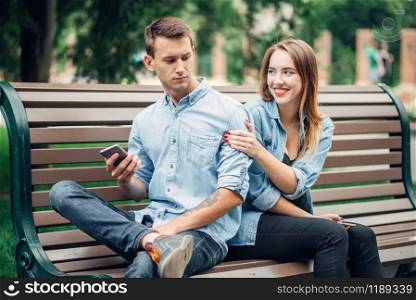 Phone addicted people, man using smartphone and ignoring his woman, couple in summer park, social addict