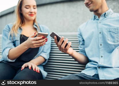 Phone addiction, addict couple sitting on the bench and looking on smartphones, social addicted people