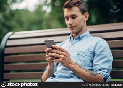Phone addiction, addict man using smartphone on the bench in park, social addicted people. Phone addiction, addict man using smartphone