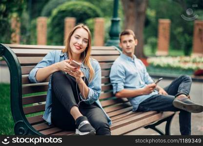 Phone addiction, couple ignoring each other on the bench in park. Man and woman using their smartphones, social addicted people