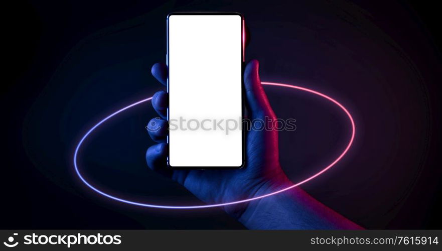 Phone in hand. Silhouette of male hand holding bezel-less smartphone with futuristic neon light circle on dark background. Screen is cut with clipping path.. Phone in hand