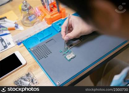 Phone repair concept a bare hand holding tweezers gripping a tiny part in a circuit board carefully and precisely on the wooden desk.