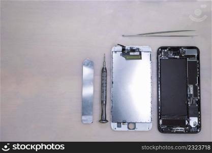 Phone repair concept the components of the smartphone separated into parts nearby the stainless tools including tweezers, an iron bar, and a tiny screwdriver.