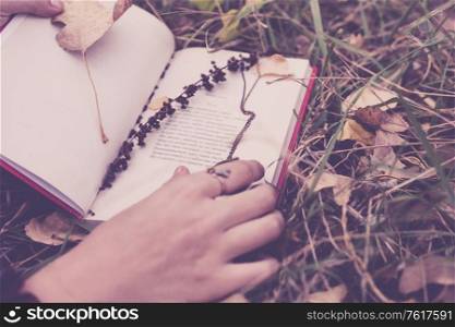 Photo an uncovered volume of poetry in the autumn grass. The book is held by a young girl&rsquo;s hands, a sprig of autumn grass is embedded in the book. The photo is toned in a retro mood.. Photo an uncovered volume of poetry in the autumn grass.