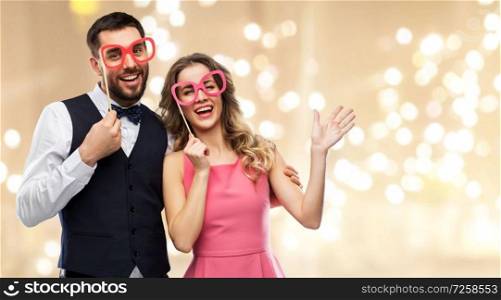 photo booth, fun and people concept - happy couple posing with party props over festive lights background. couple with party props having fun and posing