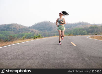 Photo fone view Asia young smiling woman runner running on asphalt road, female in sport cloth and wear a hat jogging, Healthy lifestyle concept