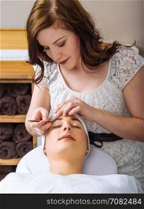 Photo of a beautician plucking the eyebrows of a young woman in a spa.