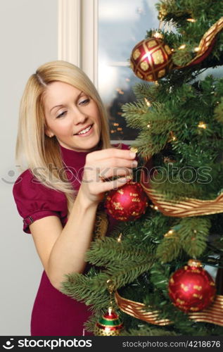 Photo of a beautiful blond female hanging ornaments on a Christmas tree.