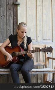 Photo of a beautiful blond female playing her acoustic guitar on an old wooden bench.