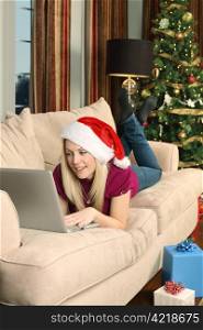 Photo of a beautiful blond female sitting on a couch using a laptop to shop for Christmas gifts.