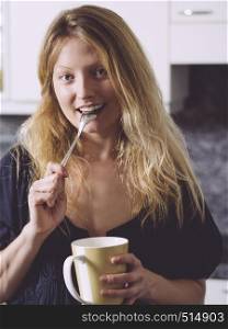 Photo of a beautiful blond holding a large coffee and a spoon in her mouth.