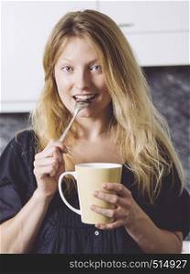 Photo of a beautiful blond holding a large coffee in her kitchen.