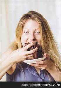 Photo of a beautiful blond woman in her early thirties with log blond hair eating a large piece of brownie or cake.