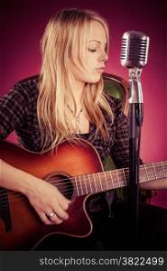 Photo of a beautiful blond woman playing an acoustic guitar. Filtered to have a vintage look.