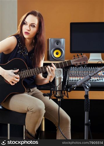 Photo of a beautiful brunette in a recording studio recording her guitar tracks.&#xA;